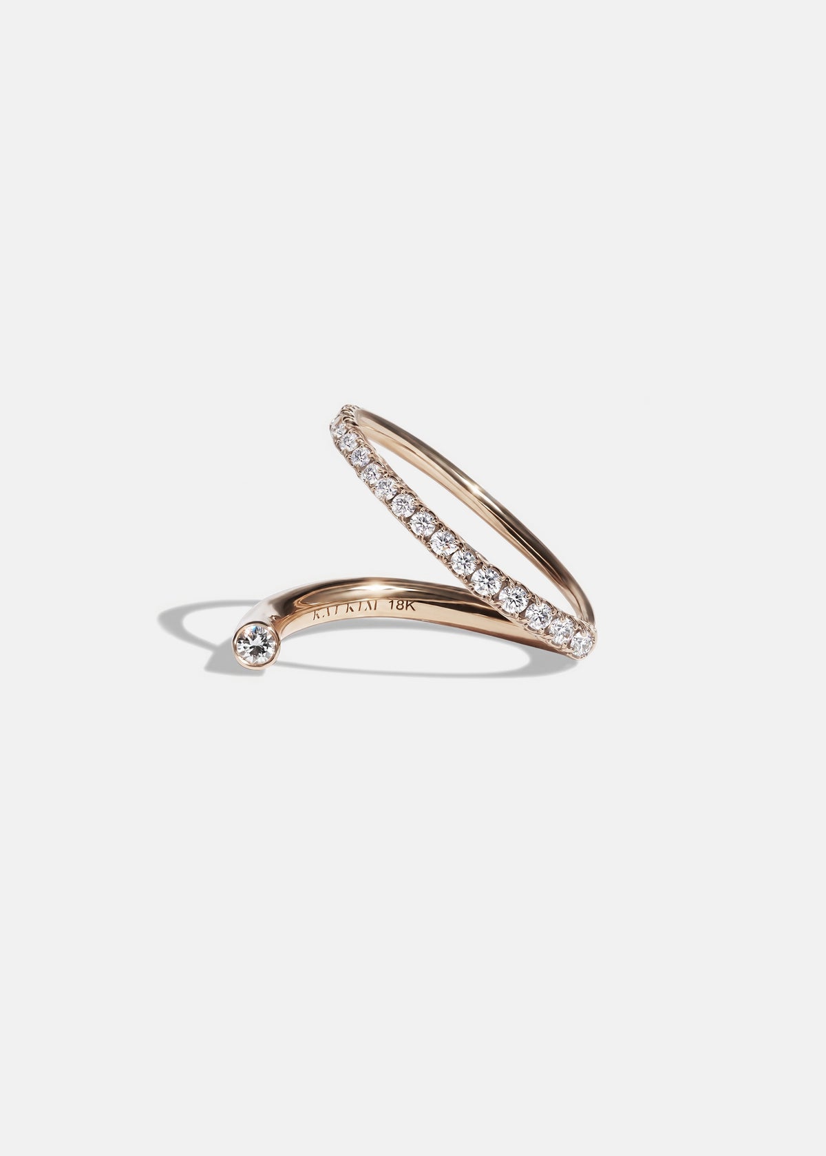 18k rose gold wrapping ring with an accent floating diamond and a subtle tilted band with pavé diamonds.
