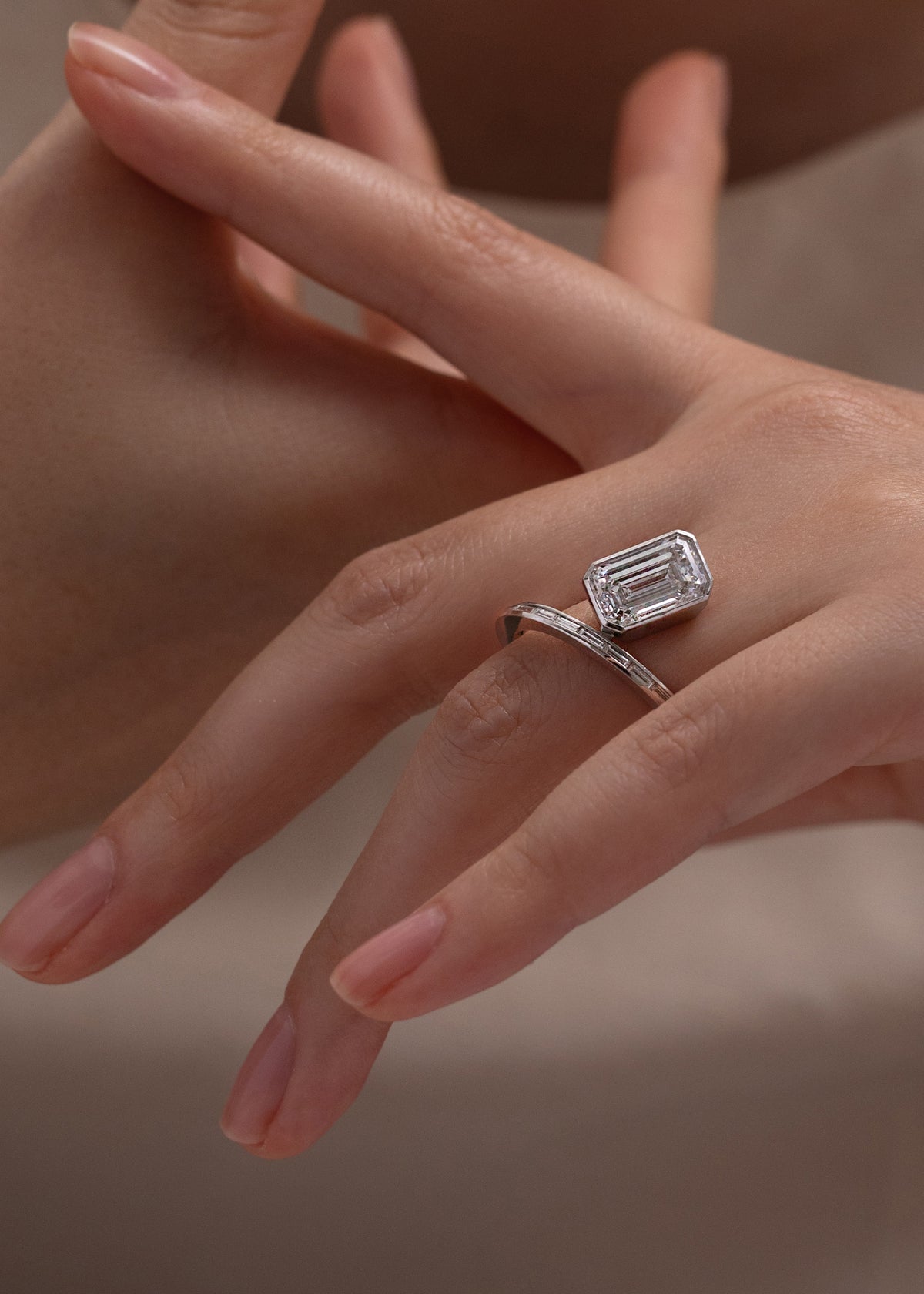 18k yellow gold bypass ring featuring a floating emerald cut diamond and tapering channel of baguettes band-close up of hand wearing it on ring finger
