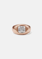 A 18k rose gold signet ring featuring a large, bezel-set asscher cut diamond, against a clean background.