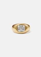 A 18k yellow gold signet ring featuring a large, bezel-set asscher cut diamond, against a clean background.