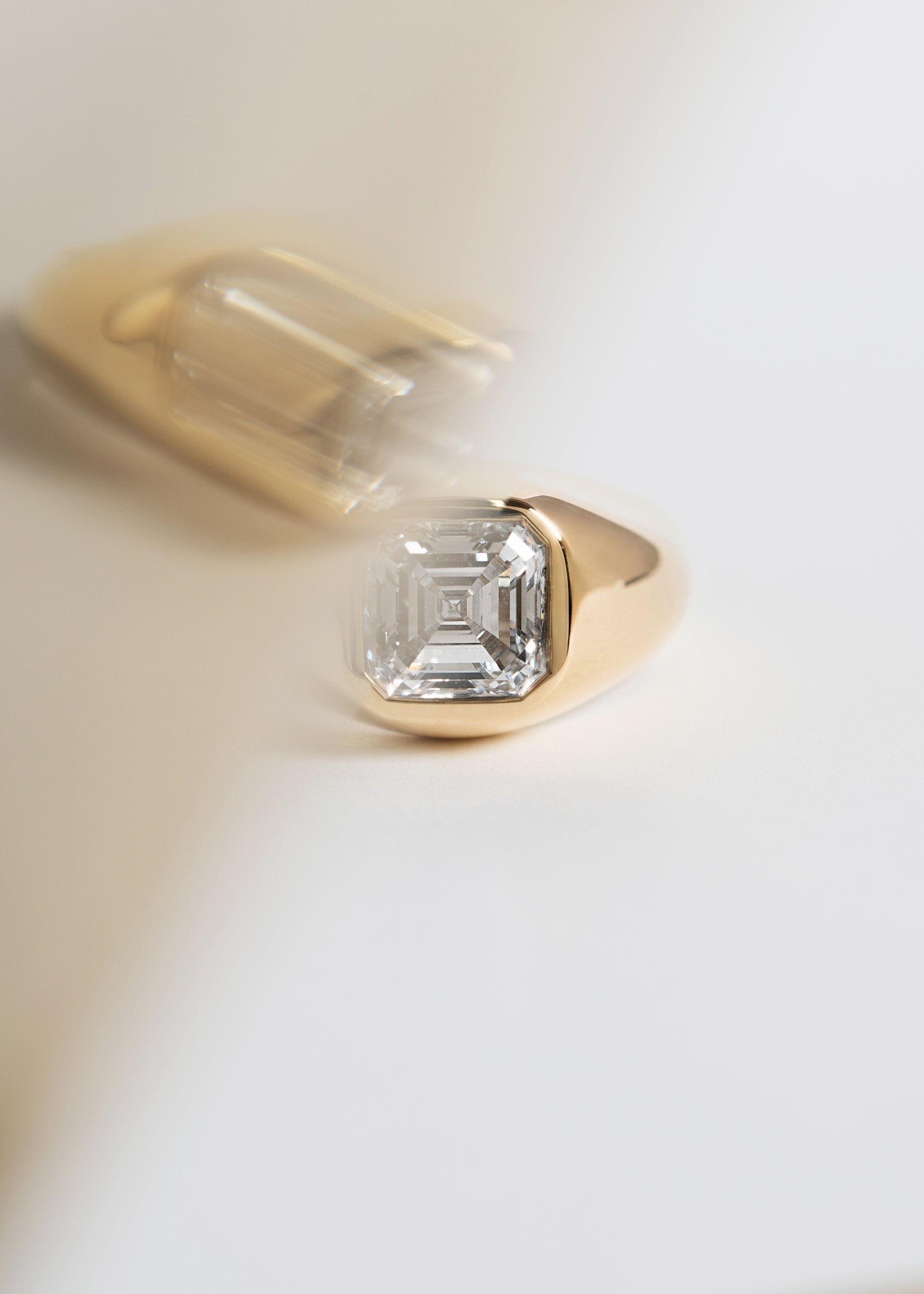 A 18k yellow gold signet ring featuring a large, bezel-set asscher cut diamond, against a clean background.