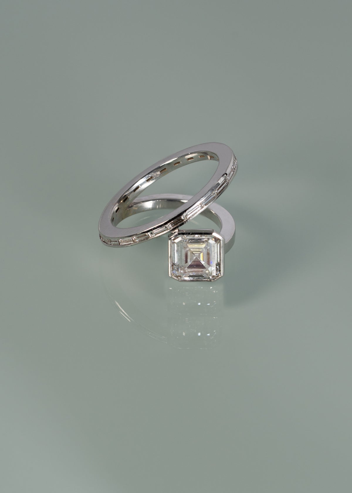 18k white gold bypass ring featuring a floating asscher cut diamond and tapering channel of baguettes band- against sea foam reflective background