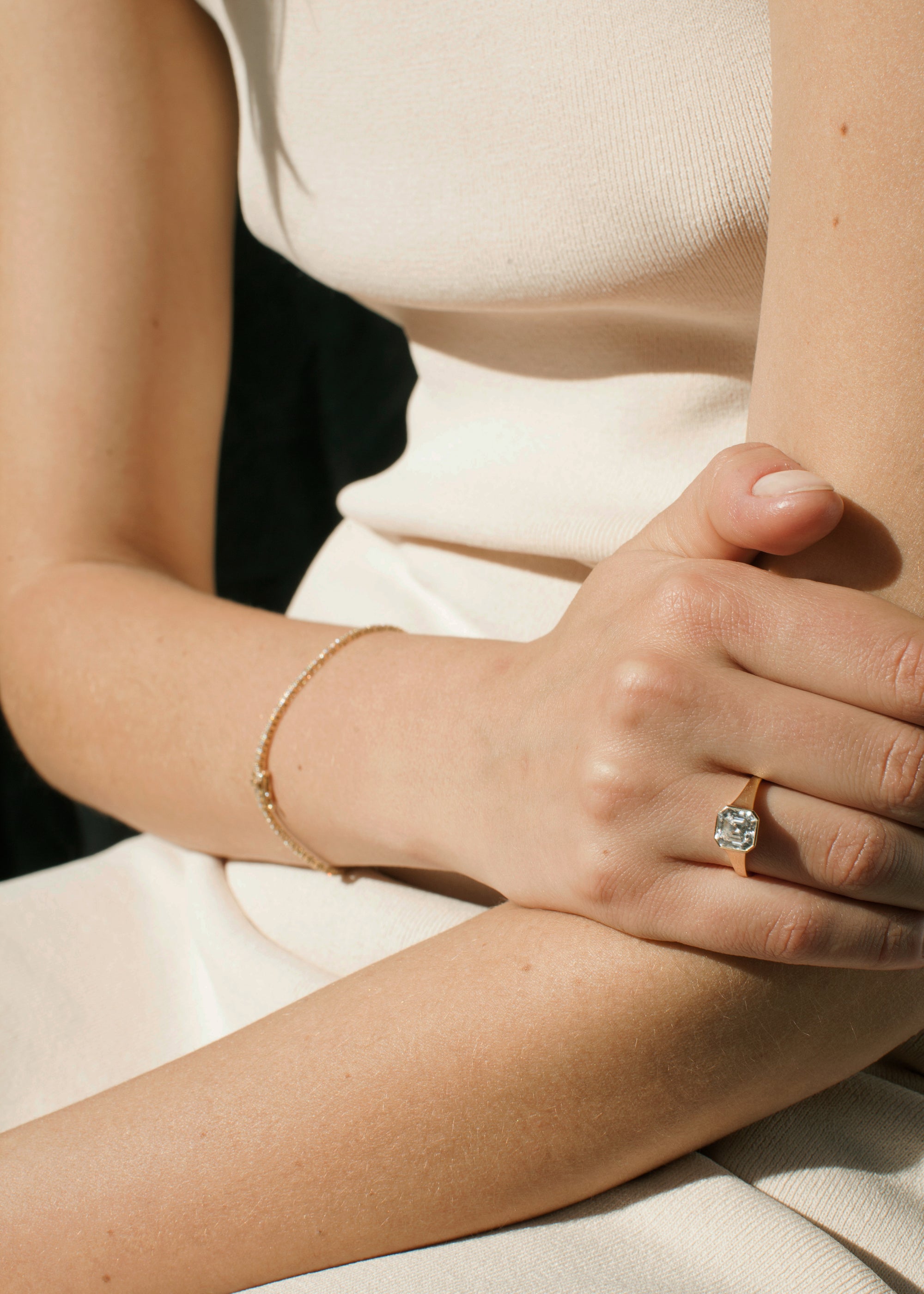 Close-up of the model's arm and hand wearing a tapering gold band with an asscher cut diamond