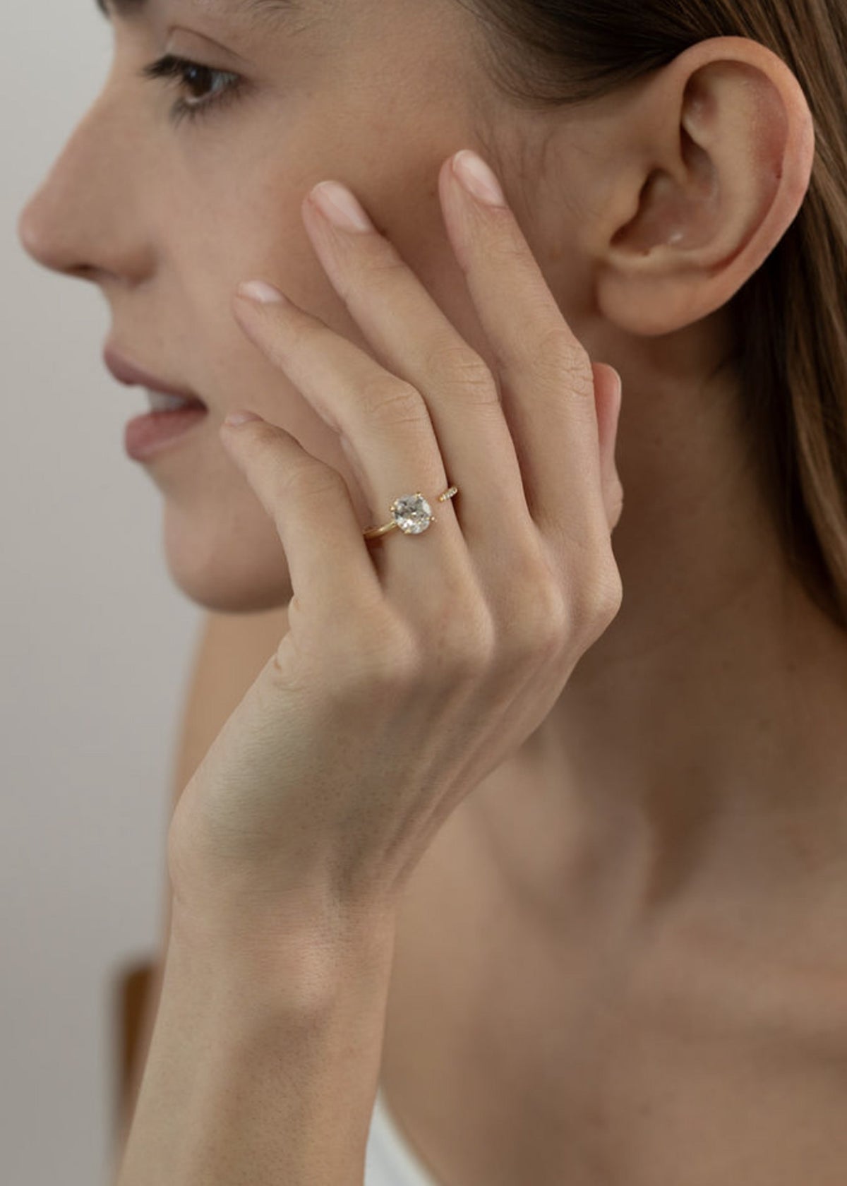 model wearing 18k yellow gold solitaire engagement ring featuring a floating round brilliant diamond on a fluid, tapering open band on her ring finger