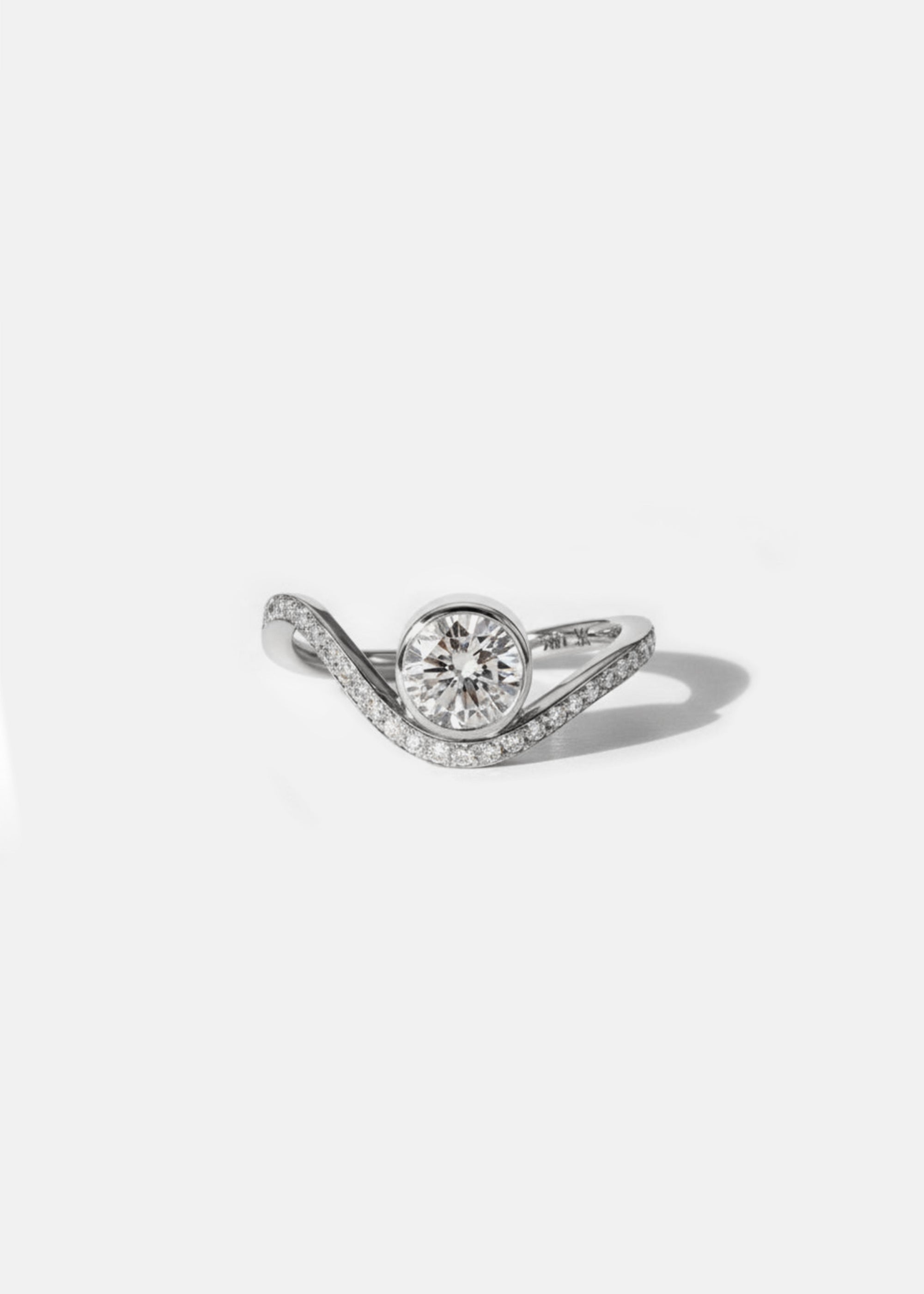 A 18k white gold ring with a wavy band design with pavé diamonds featuring a round brilliant-cut center stone.