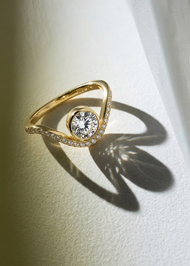 A 18k yellow gold ring with a wavy band design with pavé diamonds featuring a round brilliant-cut center stone.