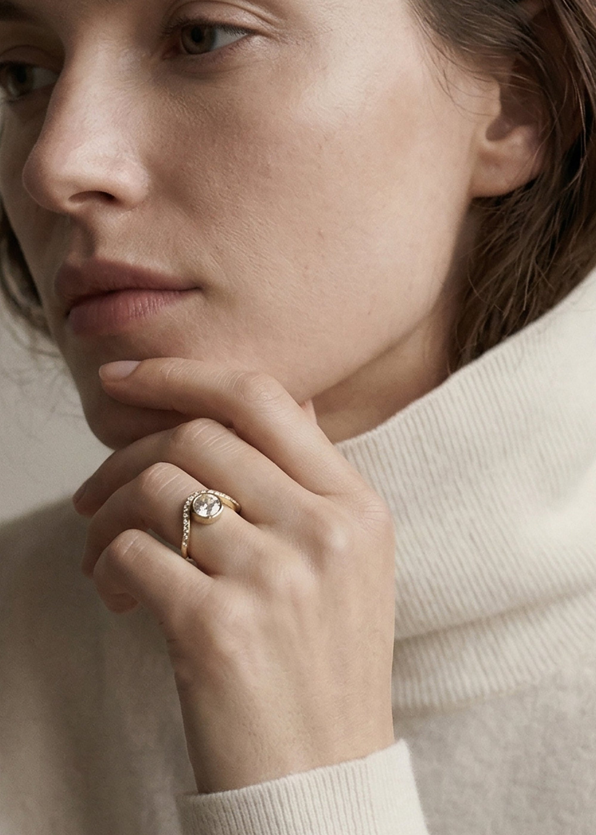 model wearing a 18k yellow gold ring with a wavy band design with pavé diamonds featuring a round brilliant-cut center stone.