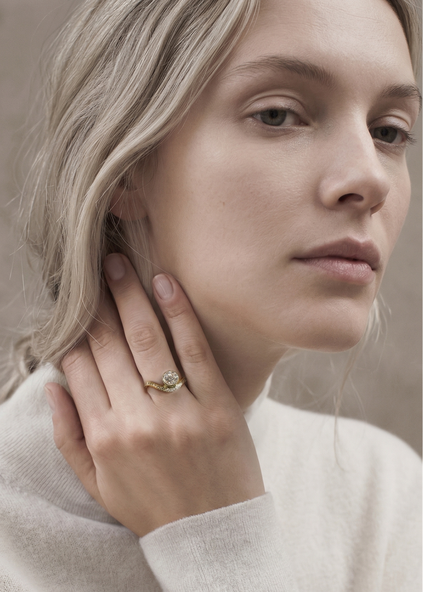 model wearing a 18k yellow gold ring with a wavy band design with pavé diamonds featuring a round brilliant-cut center stone.