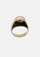 A tapering gold band with a oval cut diamond as center stone against a backlit background.