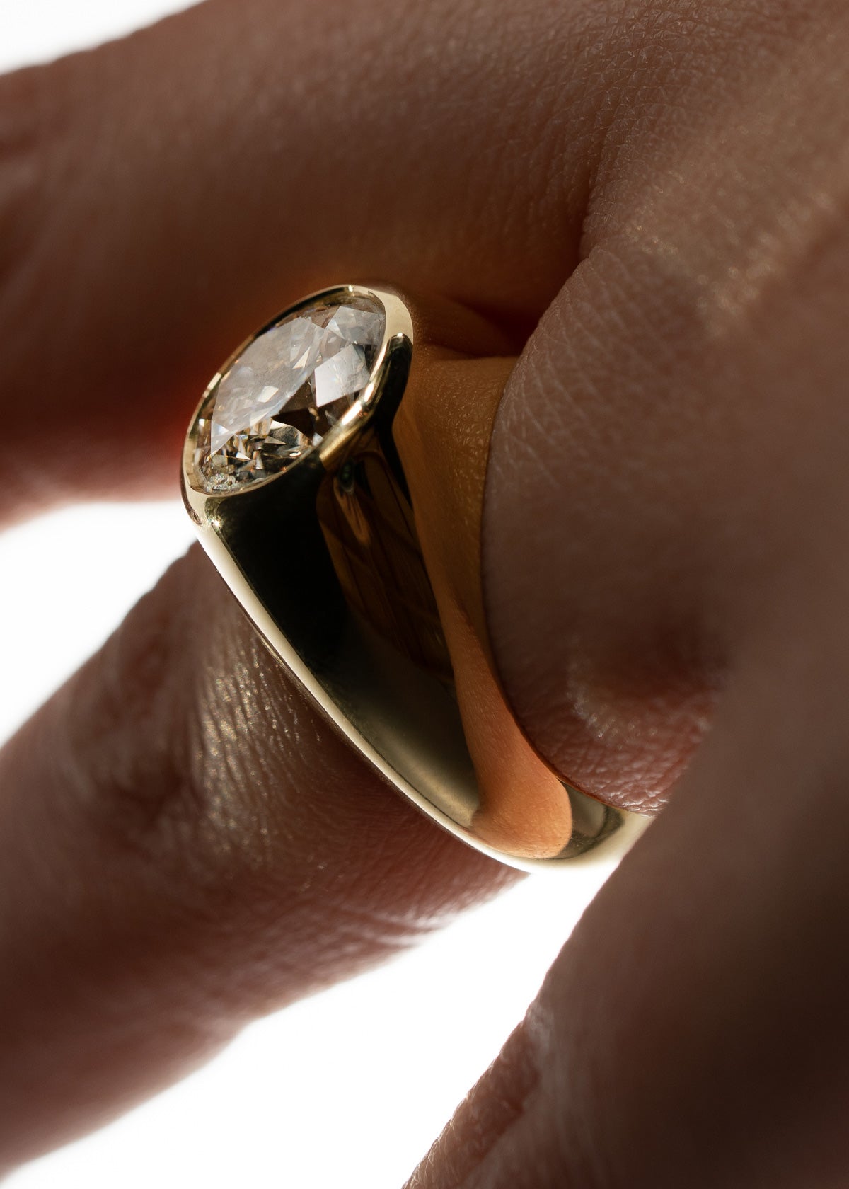 a close up of a hand wearing a gold tapering band with an oval cut diamond as the center stone.