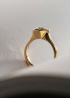 close up of 18k yellow gold architectural engagement ring with a round cut diamond in a thick, octagon bezel setting.