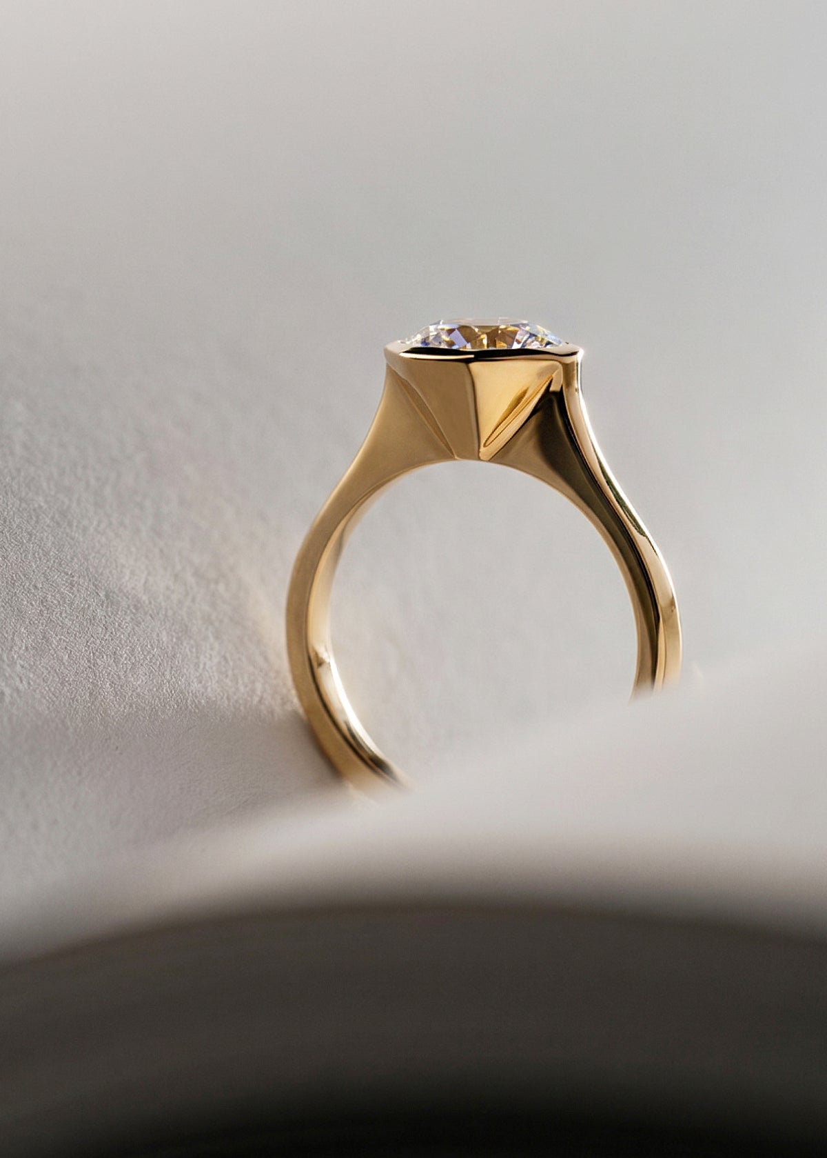 close up of 18k yellow gold architectural engagement ring with a round cut diamond in a thick, octagon bezel setting.