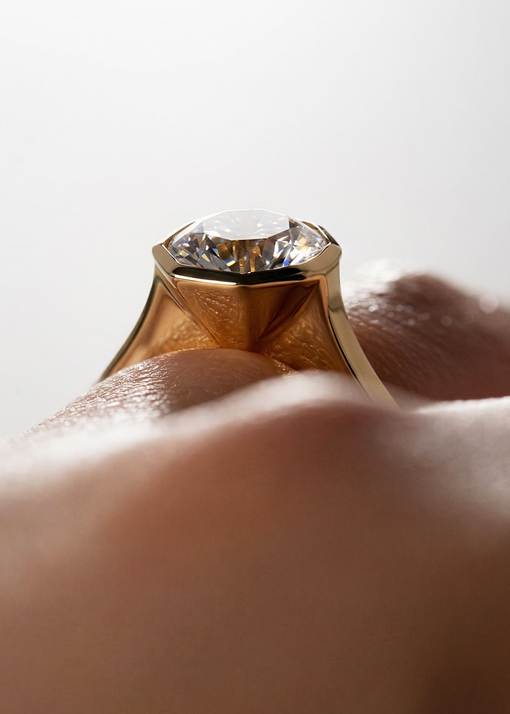 close up of 18k yellow gold architectural engagement ring with a round cut diamond in a thick, octagon bezel setting.