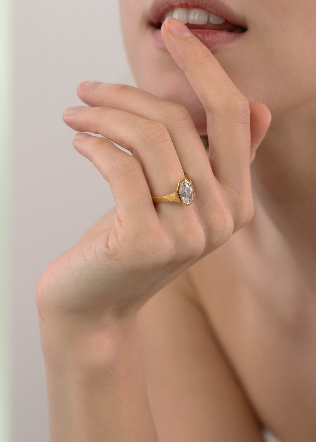 closeup of a hand wearing a 18k yellow gold engagement ring featuring an oval cut diamond in a sculpted octagonal bezel frame.