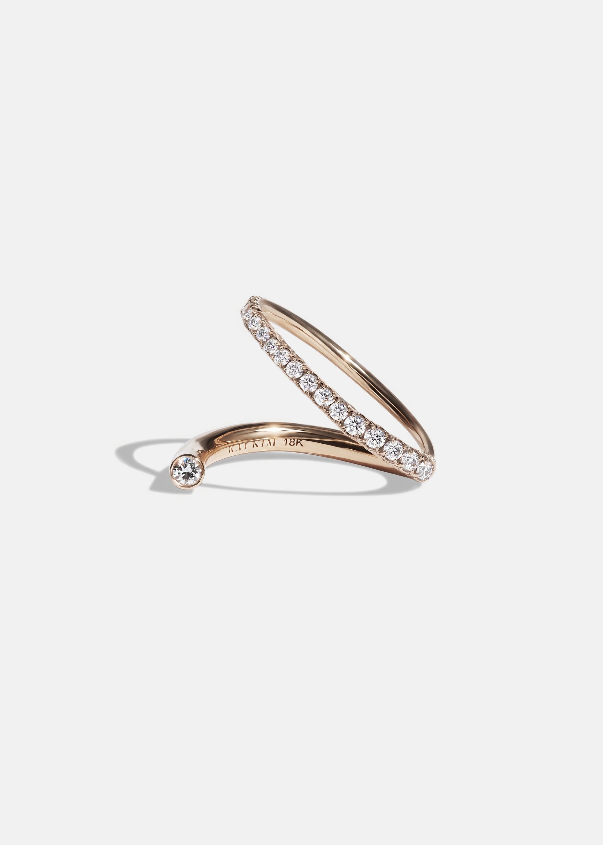 18k rose gold wrapping ring with an accent floating diamond and a subtle tilted band with pavé diamonds.