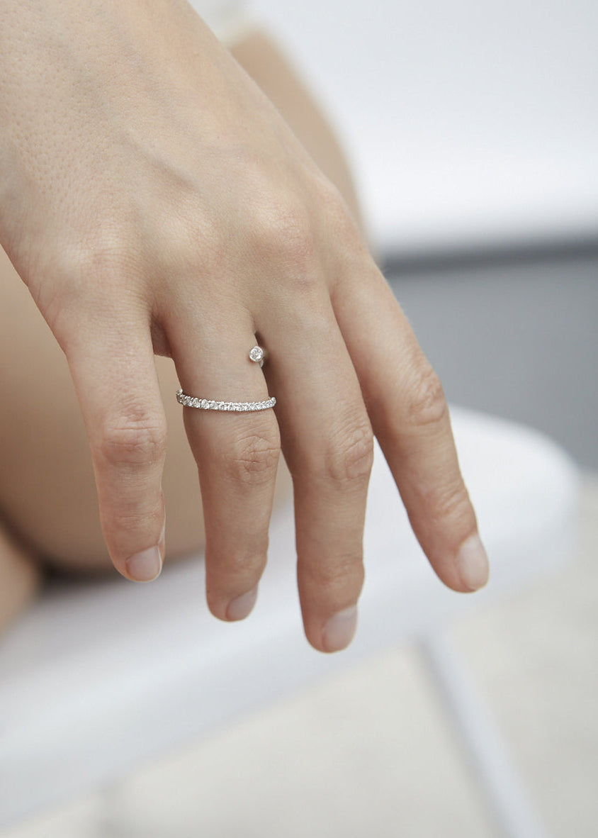 closeup of a hand wearing 18k white gold wrapping ring with an accent floating diamond and a subtle tilted band with pavé diamonds.