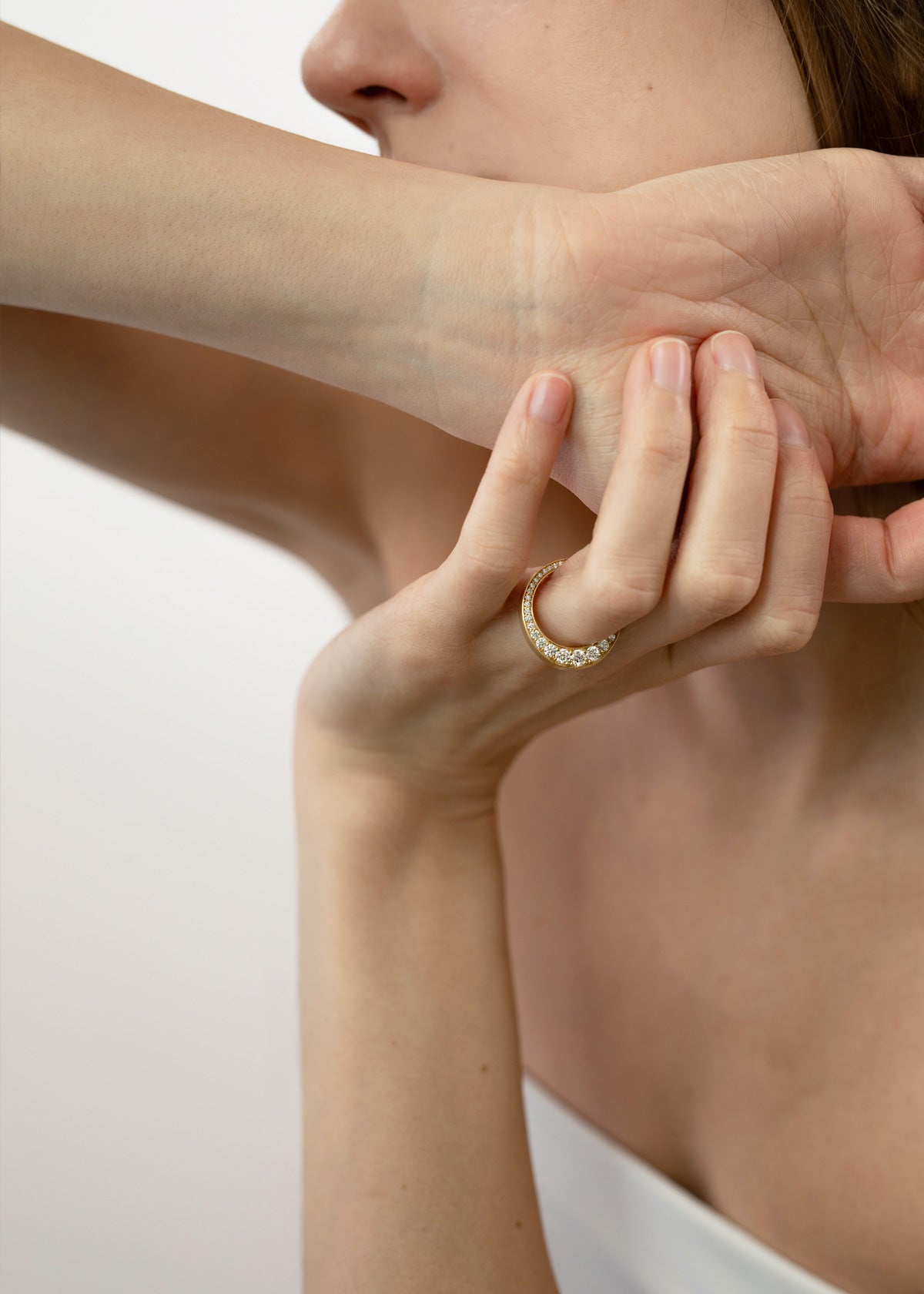 close up of a model wearing a 18k yellow gold ring featuring a tapering of round cut diamonds along the tapering gold band.
