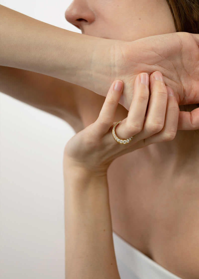 close up of a model wearing a 18k yellow gold ring featuring a tapering of round cut diamonds along the tapering gold band.