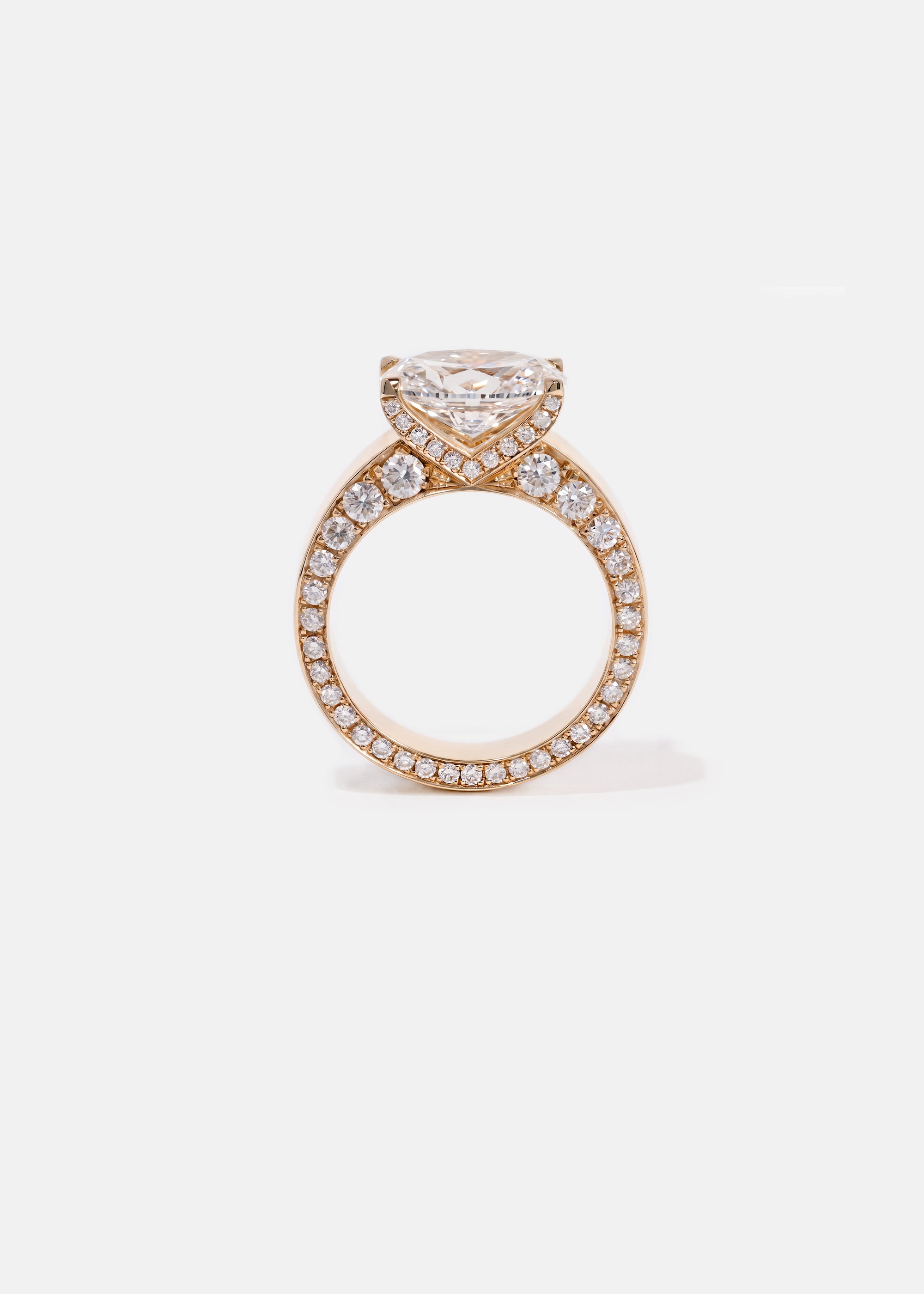 A 18k rose gold ring featuring a oval cut diamond center stone and pavé-set diamonds along the shank with tapering diamonds along the band
