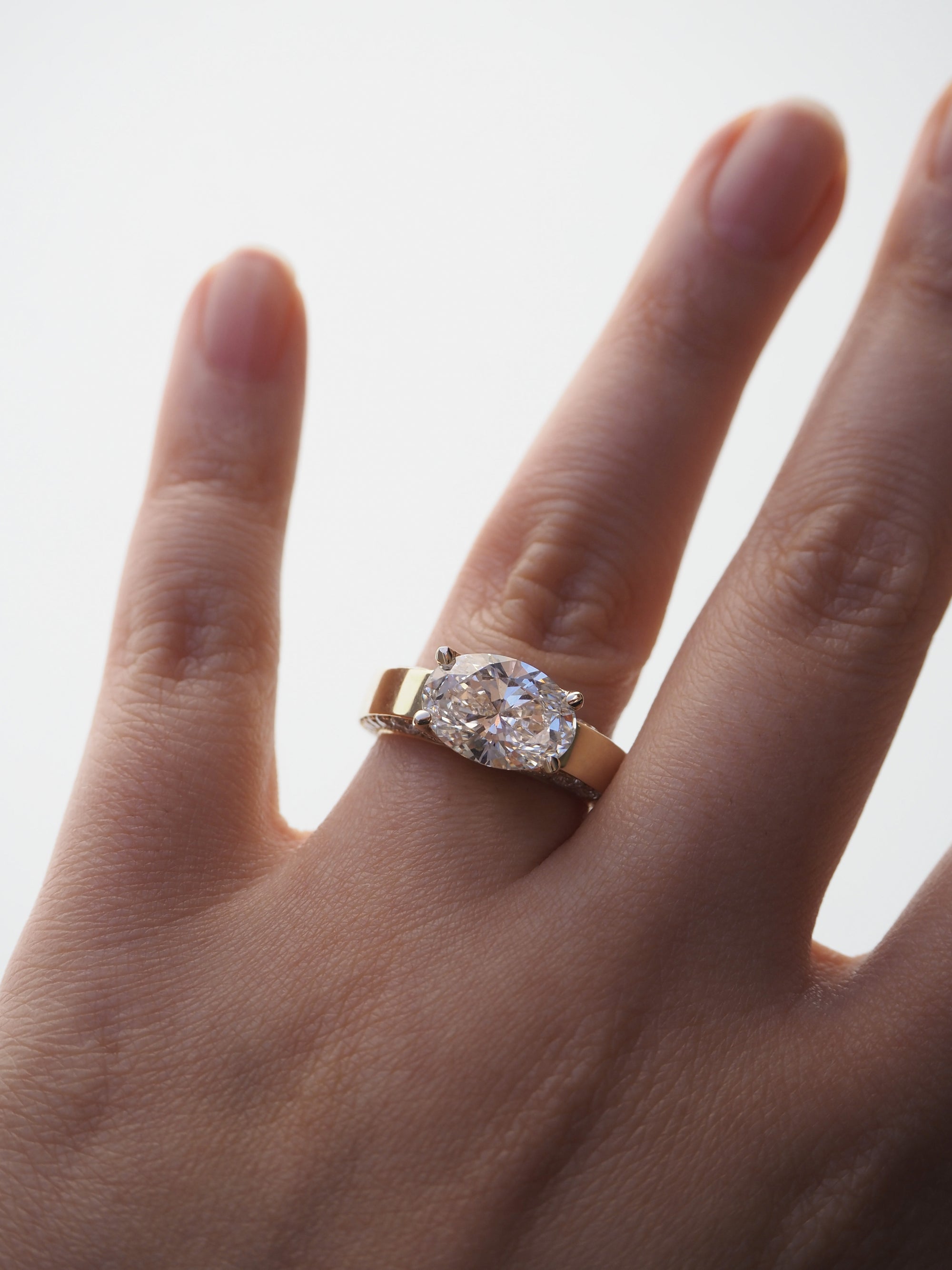 hand wearing a thick gold band with a oval cut diamond in an east west setting as the center stone