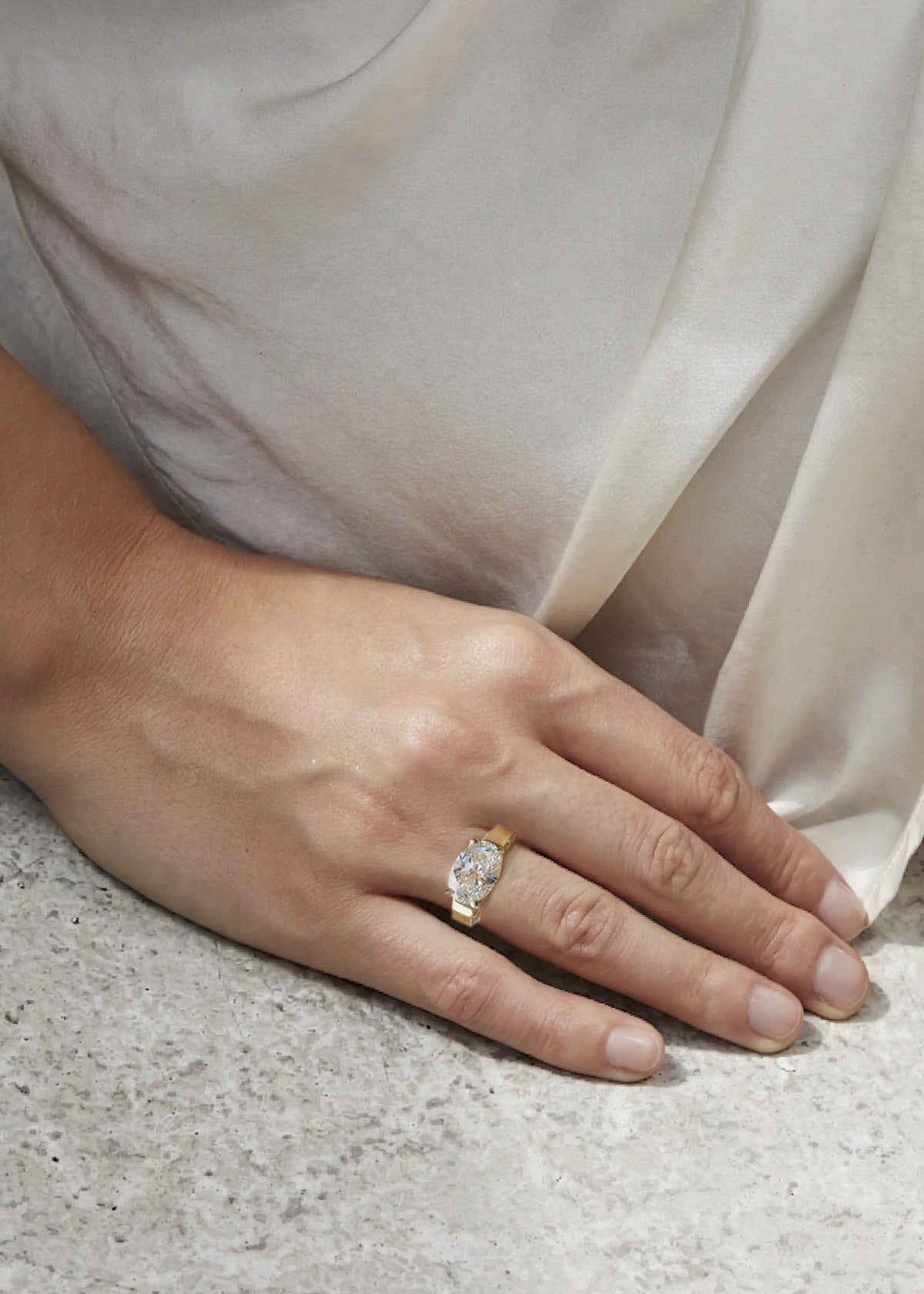 model wearing a 18k yellow gold ring featuring a oval cut diamond center stone and pavé-set diamonds along the shank with tapering diamonds along the band
