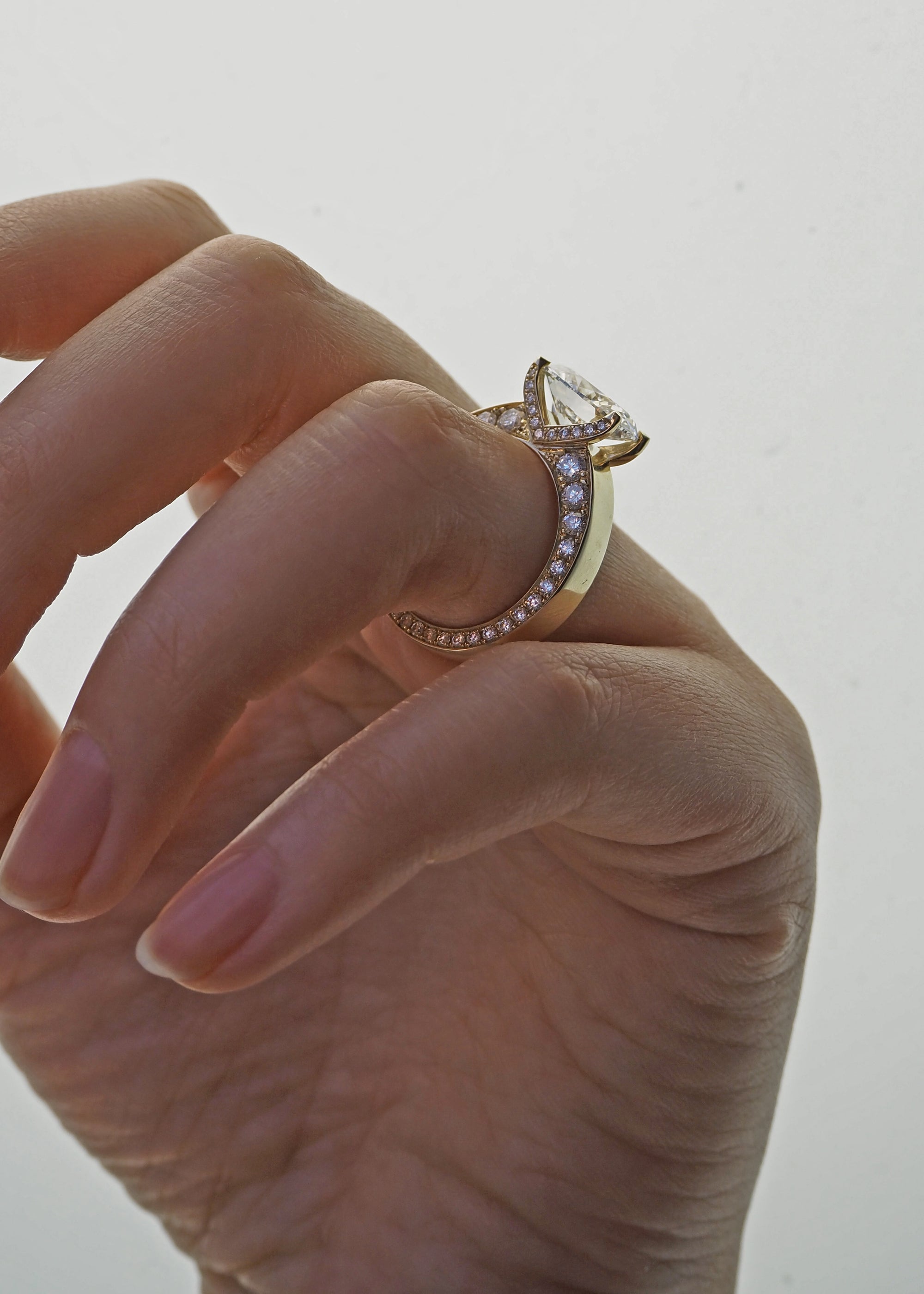 A 18k yellow gold ring featuring a oval cut diamond center stone and pavé-set diamonds along the shank with tapering diamonds along the band on a finger