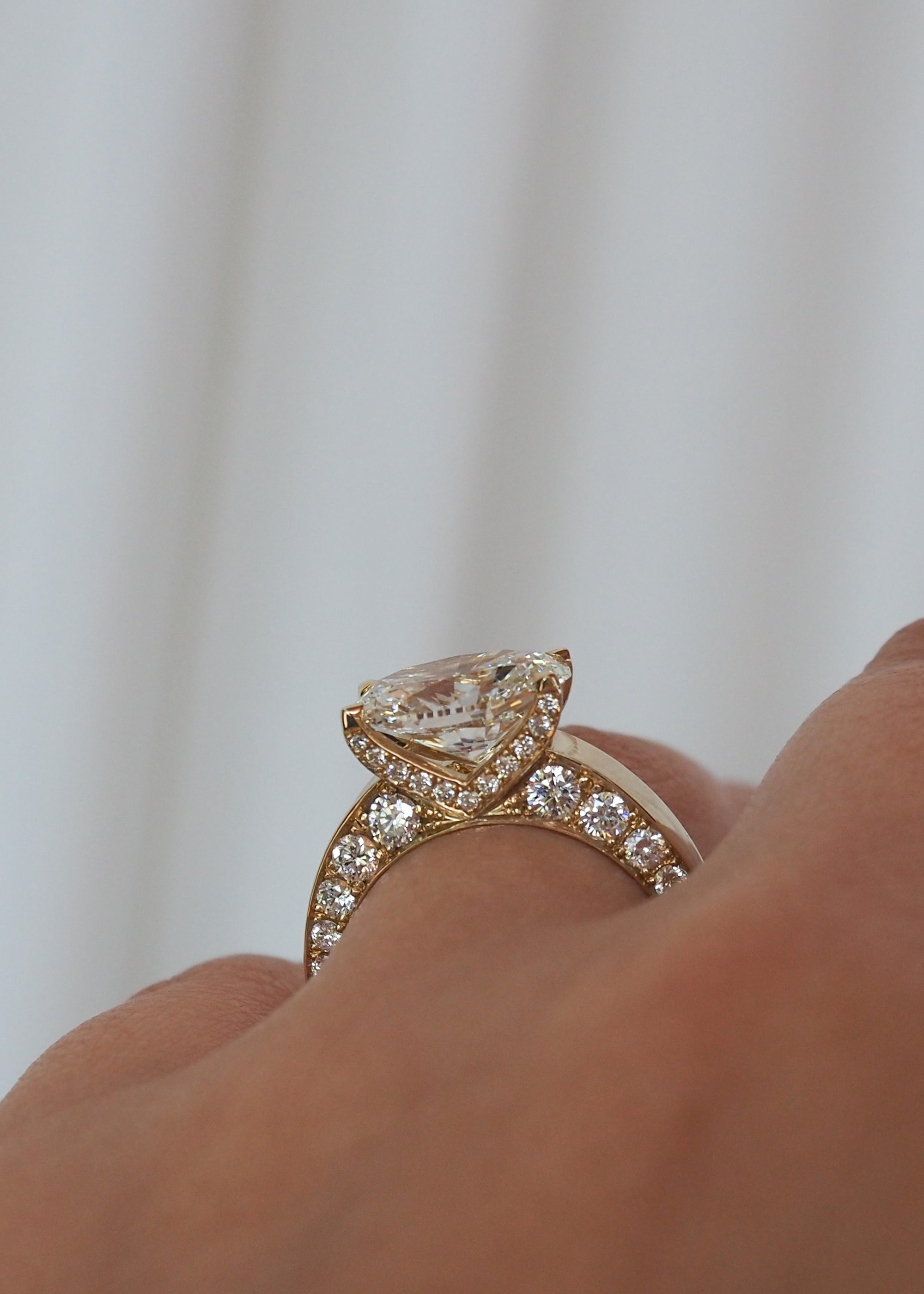 hand wearing A 18k yellow gold ring featuring a oval cut diamond center stone and pavé-set diamonds along the shank with tapering diamonds along the band