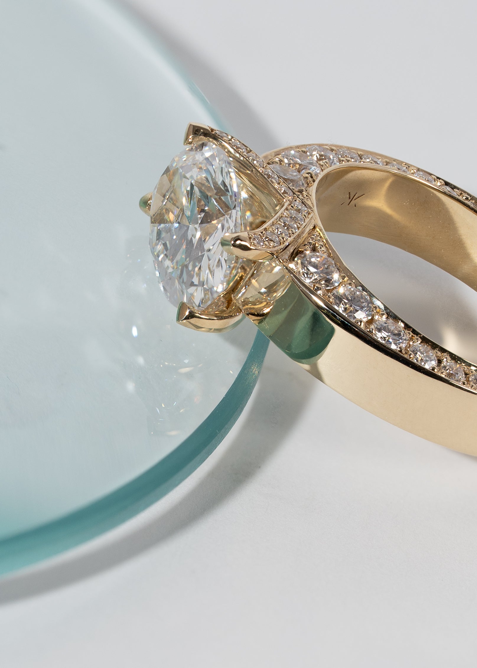 A 18k yellow gold ring featuring a oval cut diamond center stone and pavé-set diamonds along the shank with tapering diamonds along the band