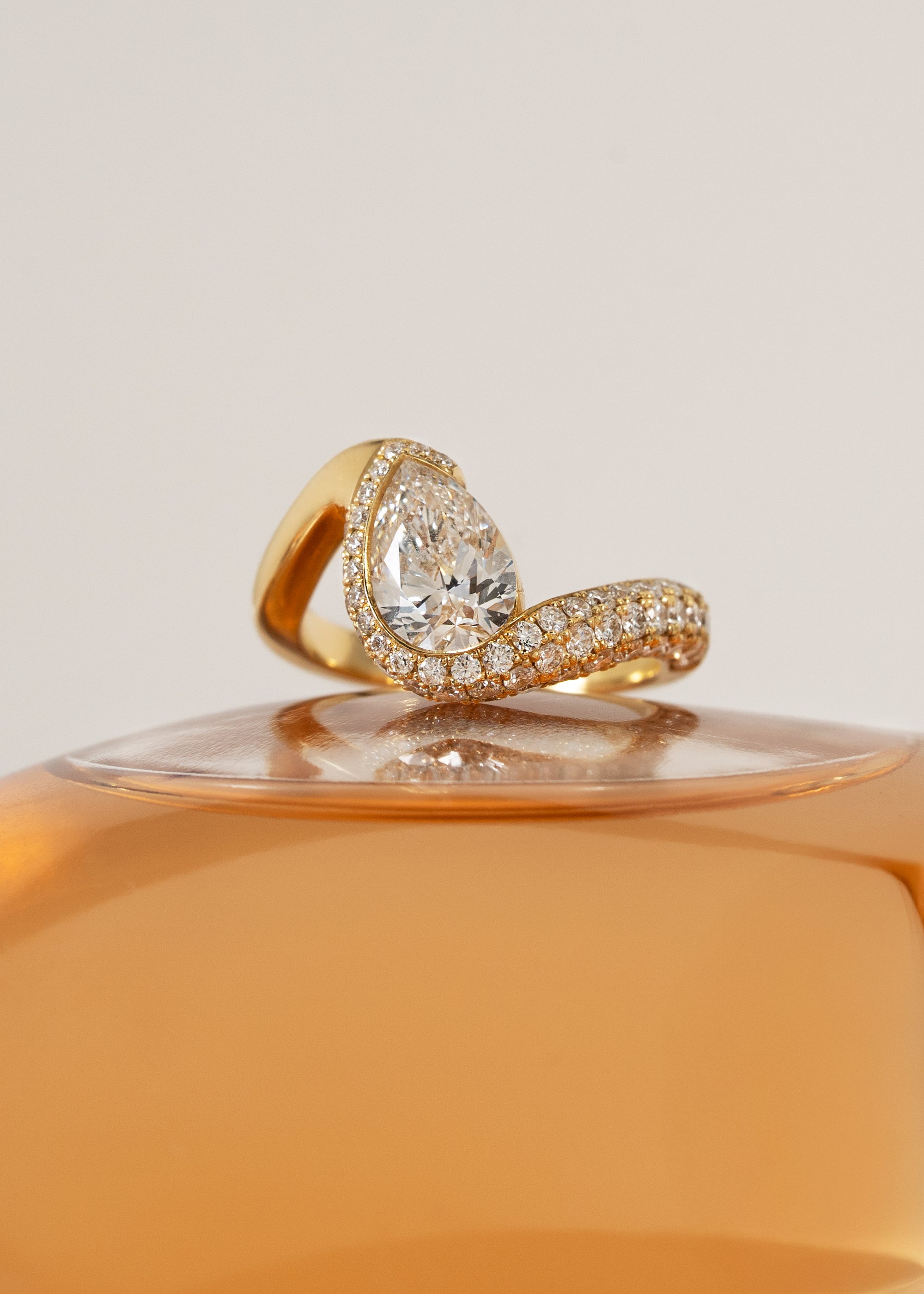  18k yellow gold ring featuring a pear-cut diamond in a curved, wave-like setting with pavé diamonds around the center stone
