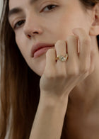 model wearing  18k yellow gold ring featuring a pear-cut diamond in a curved, wave-like setting with pavé diamonds around the center stone