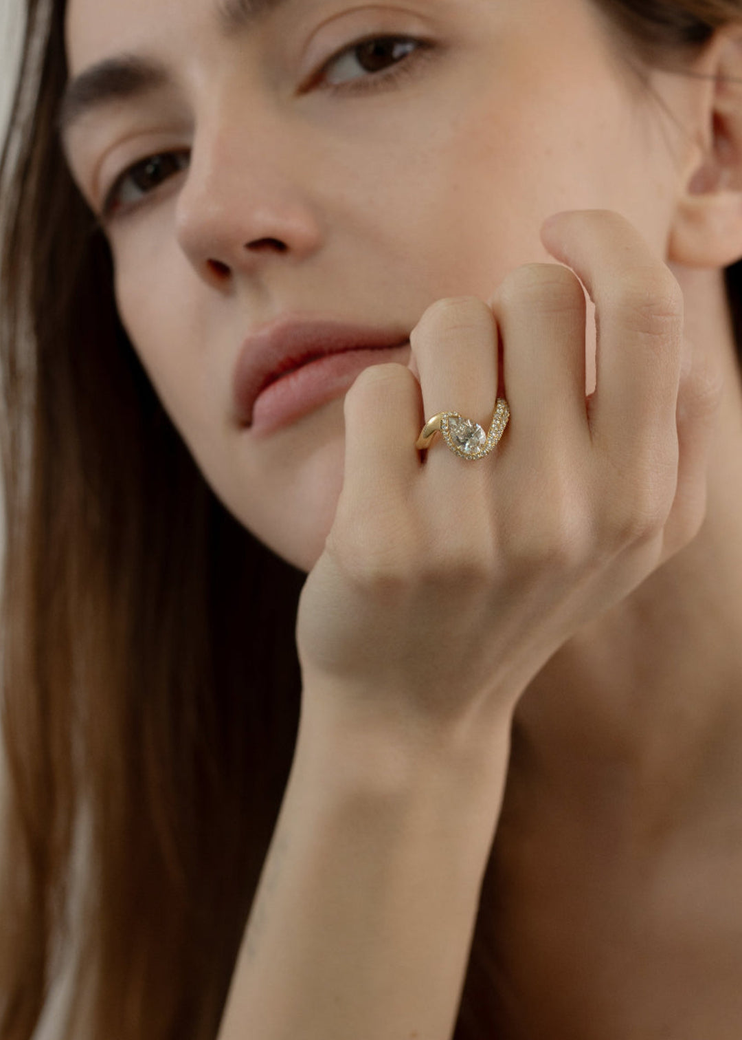 model wearing  18k yellow gold ring featuring a pear-cut diamond in a curved, wave-like setting with pavé diamonds around the center stone