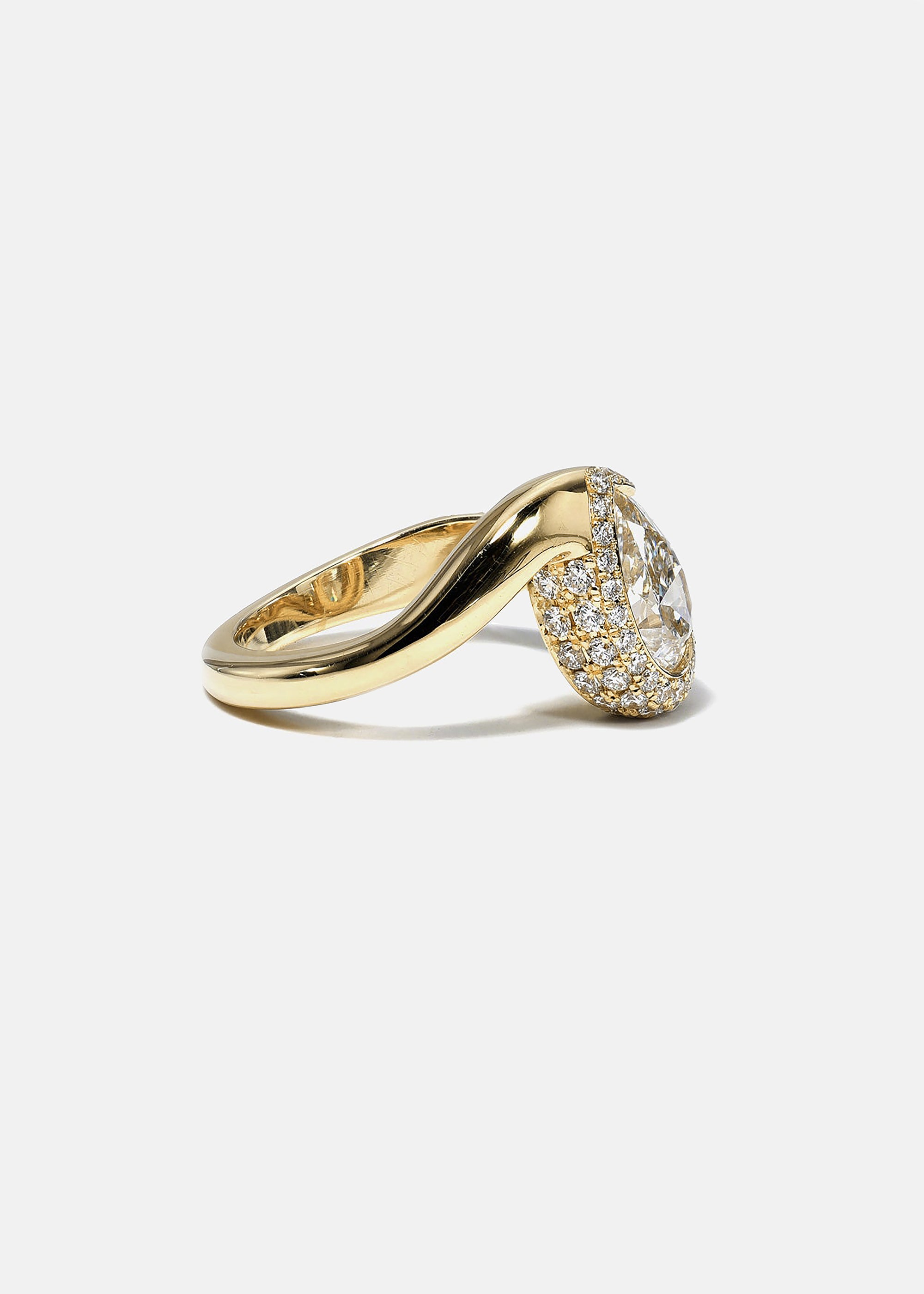 side view of  18k yellow gold ring featuring a pear-cut diamond in a curved, wave-like setting with pavé diamonds around the center stone