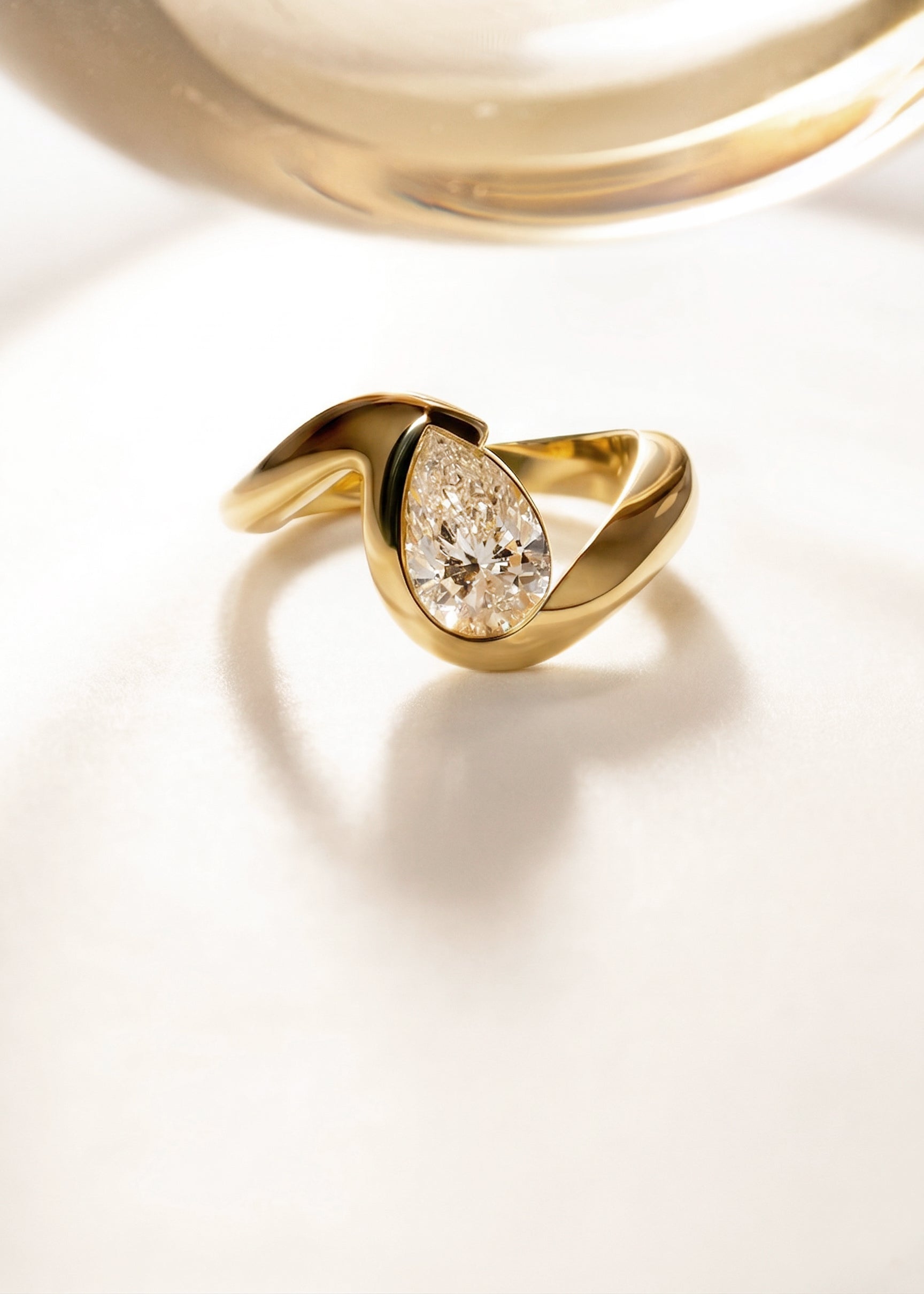 18k yellow gold ring featuring a pear-cut diamond in a curved, wave-like setting.