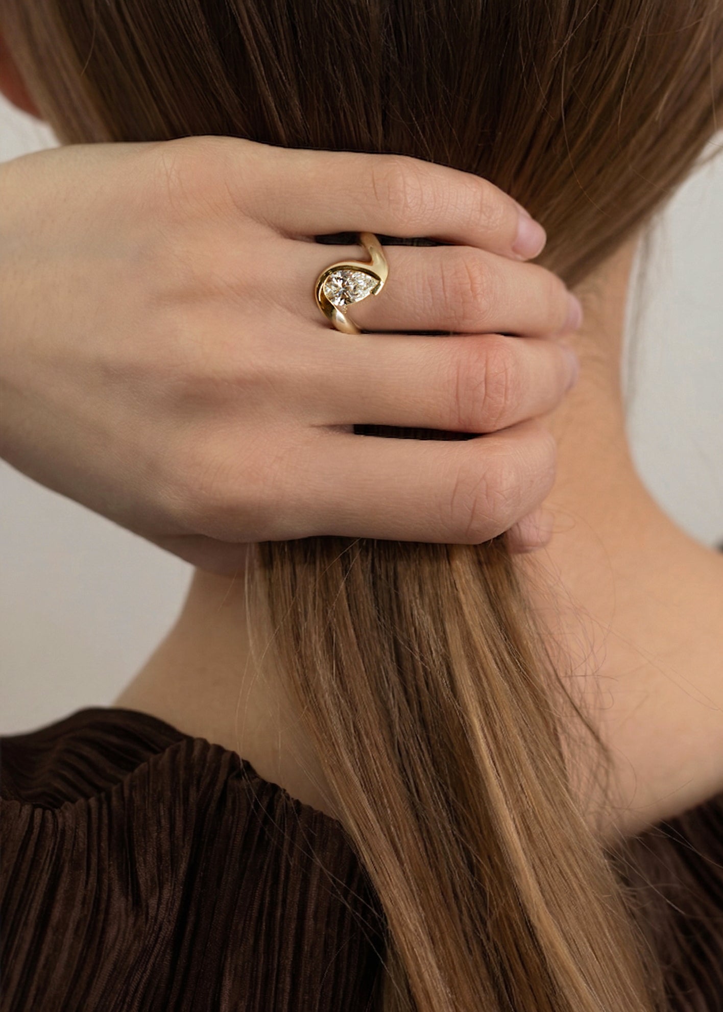model wearing 18k yellow gold ring featuring a pear-cut diamond in a curved, wave-like setting-on ring finger