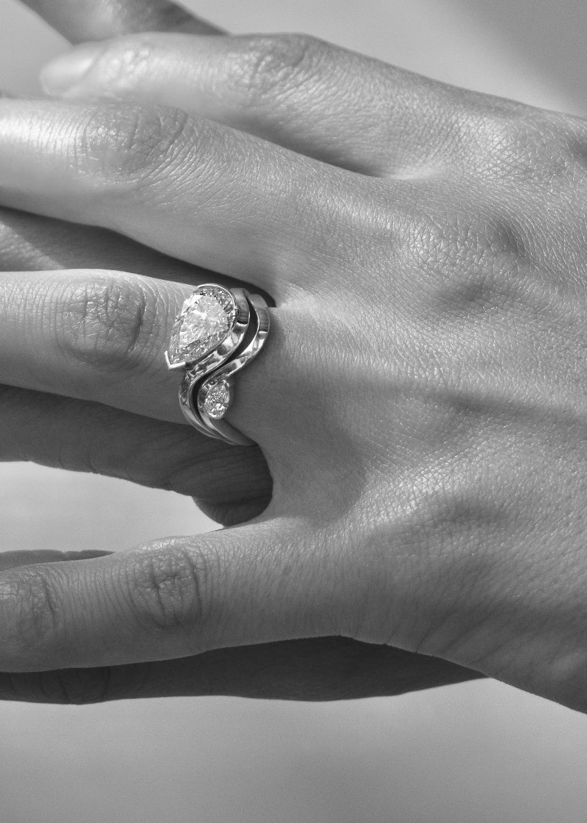 Model wearing 18k yellow gold ring- wave band with pavé diamonds paired with a gold wave band with a small pear cut diamond- pear cut diamond