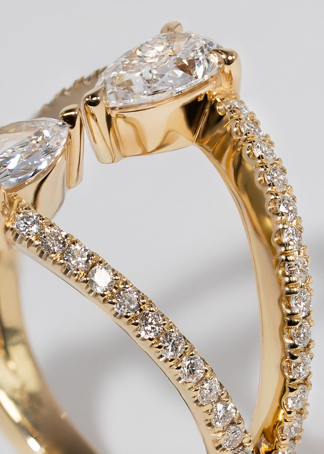close up of a 18k yellow gold dual engagement ring with two touching pear-cut diamonds facing opposite directions, with pavé diamonds along the band.