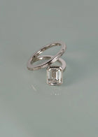 18k white gold bypass ring featuring a floating emerald cut diamond and tapering channel of baguettes band on reflective surface