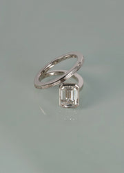 18k white gold bypass ring featuring a floating emerald cut diamond and tapering channel of baguettes band on reflective surface