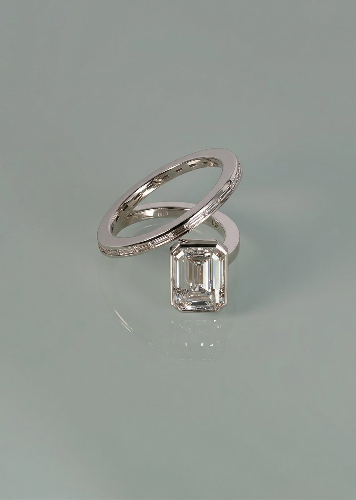 18k white gold bypass ring featuring a floating emerald cut diamond and tapering channel of baguettes band on reflective surface