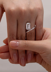 Close-up of a hand wearing an 18k white gold bypass ring featuring a floating emerald cut diamond and tapering channel of baguettes band.