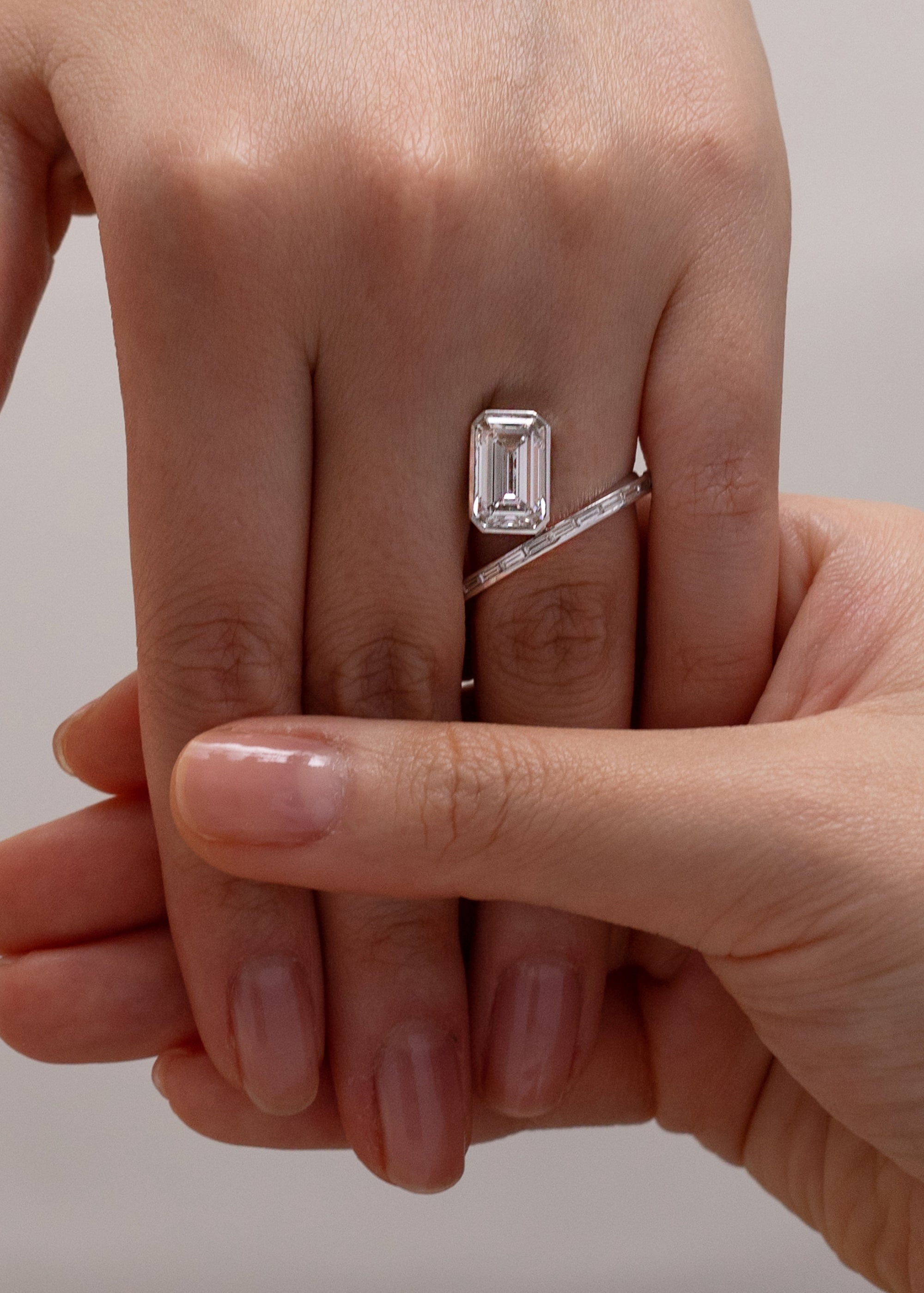 Close-up of a hand wearing an 18k white gold bypass ring featuring a floating emerald cut diamond and tapering channel of baguettes band.