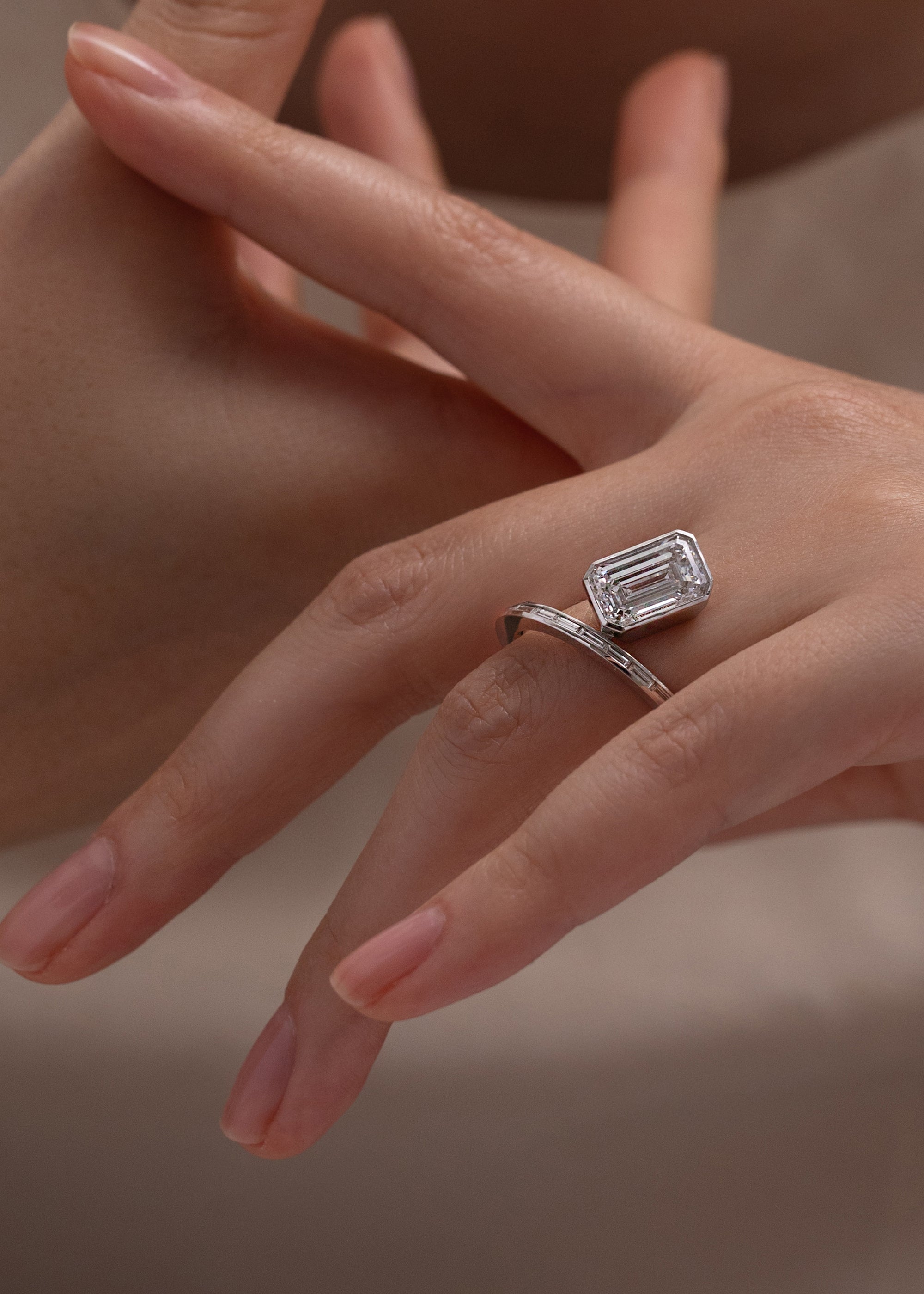 18k yellow gold bypass ring featuring a floating emerald cut diamond and tapering channel of baguettes band-close up of hand wearing it on ring finger
