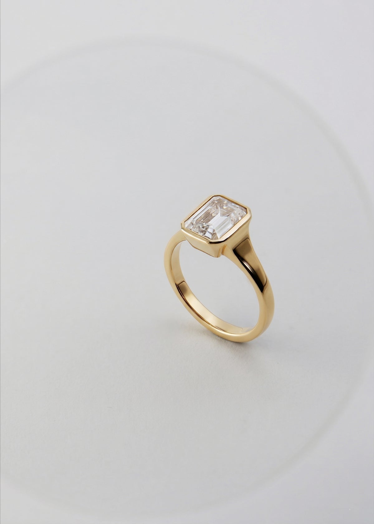 a 18k yellow gold ring with a emerald cut diamond center stone against a light grey background