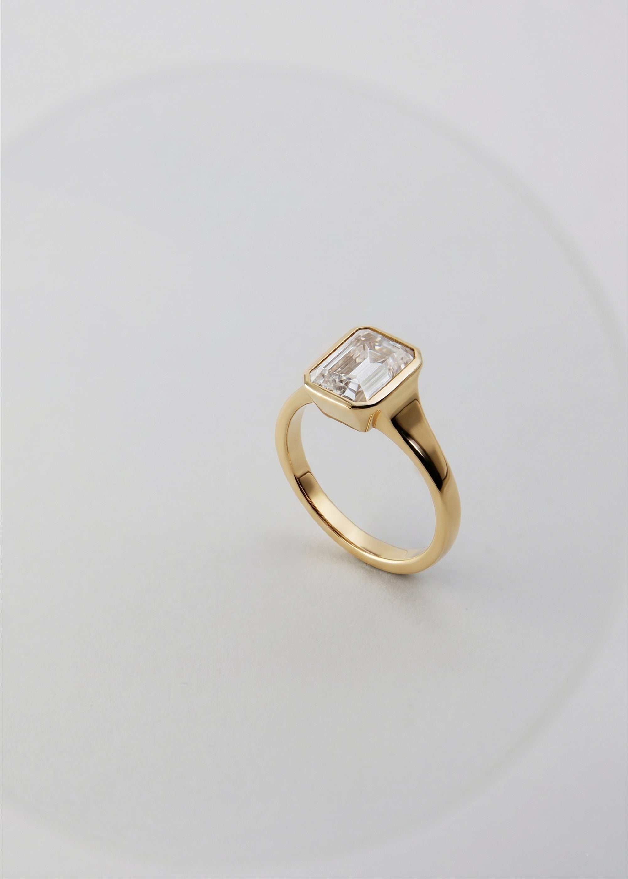 a 18k yellow gold ring with a emerald cut diamond center stone against a light grey background