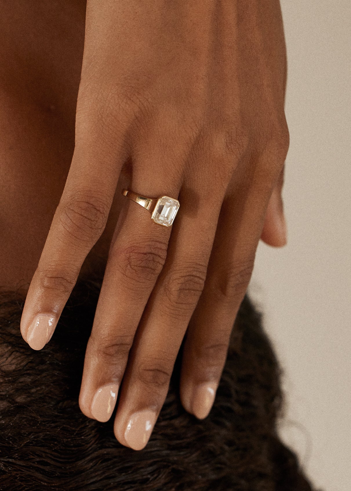 hand wearing a 18k yellow gold ring with a emerald cut diamond center stone