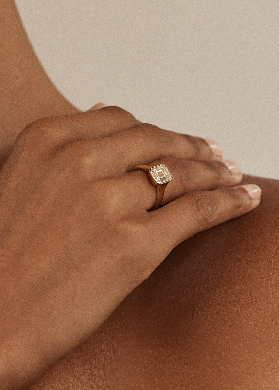 hand wearing a 18k yellow gold ring with a emerald cut diamond center stone