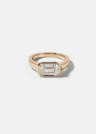 a 18k rose gold ring with a east west emerald cut diamond as the center stone
