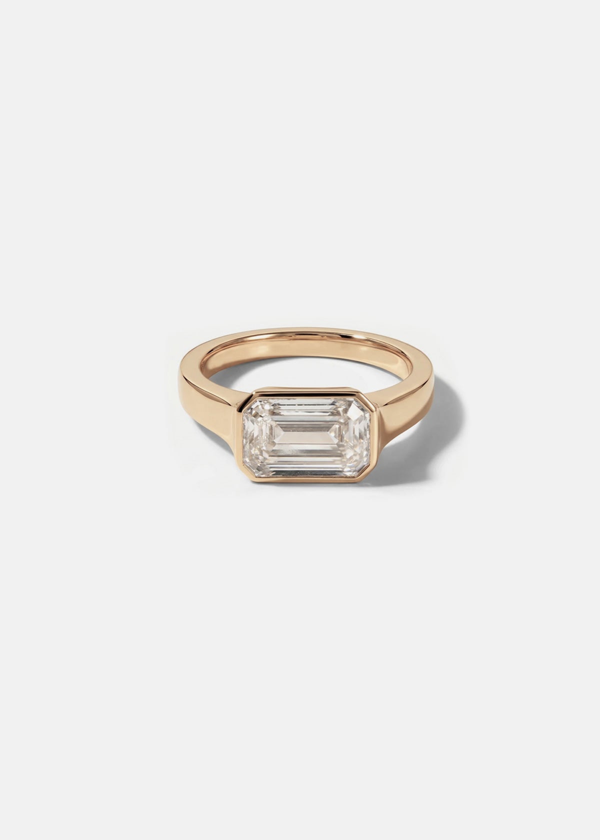 a 18k rose gold ring with a east west emerald cut diamond as the center stone