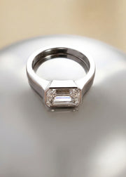 a 18k white gold ring with a east west emerald cut diamond as the center stone on a reflective surface
