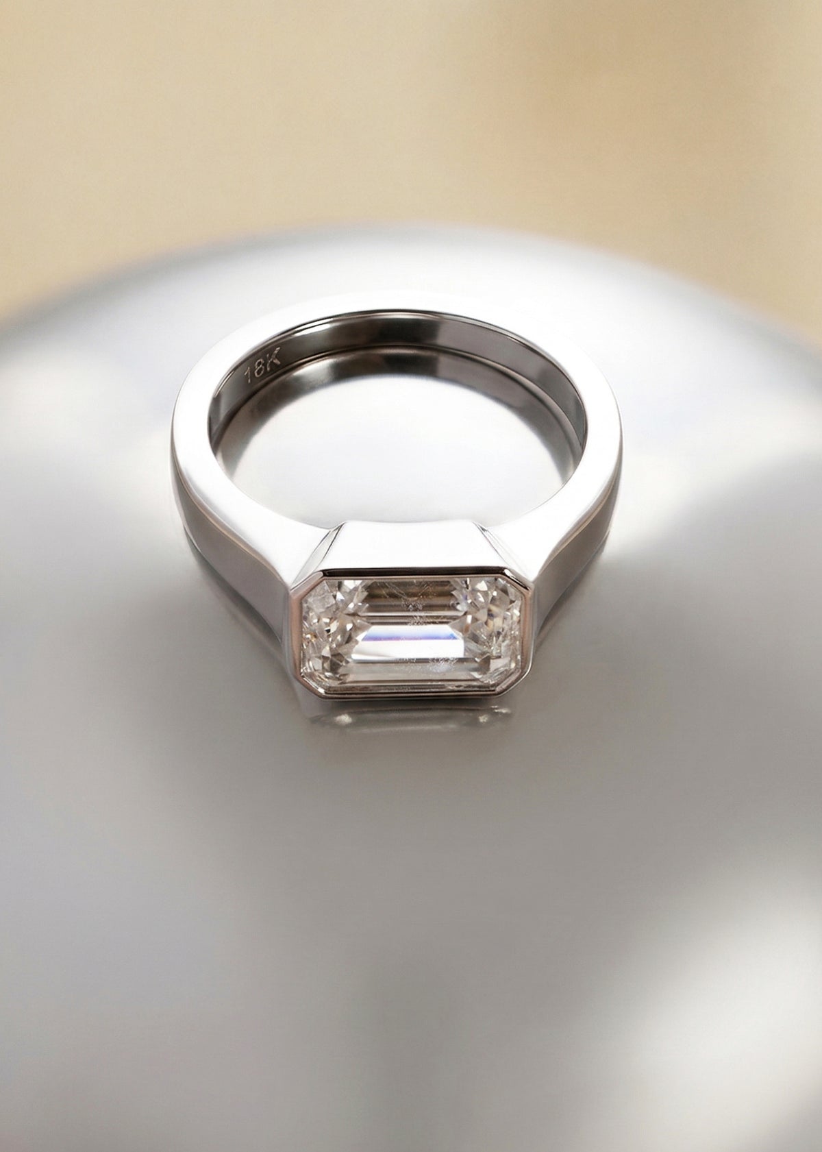 a 18k white gold ring with a east west emerald cut diamond as the center stone on a reflective surface